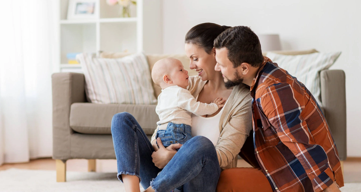 A man and woman are sitting on the floor with their baby in the living room.